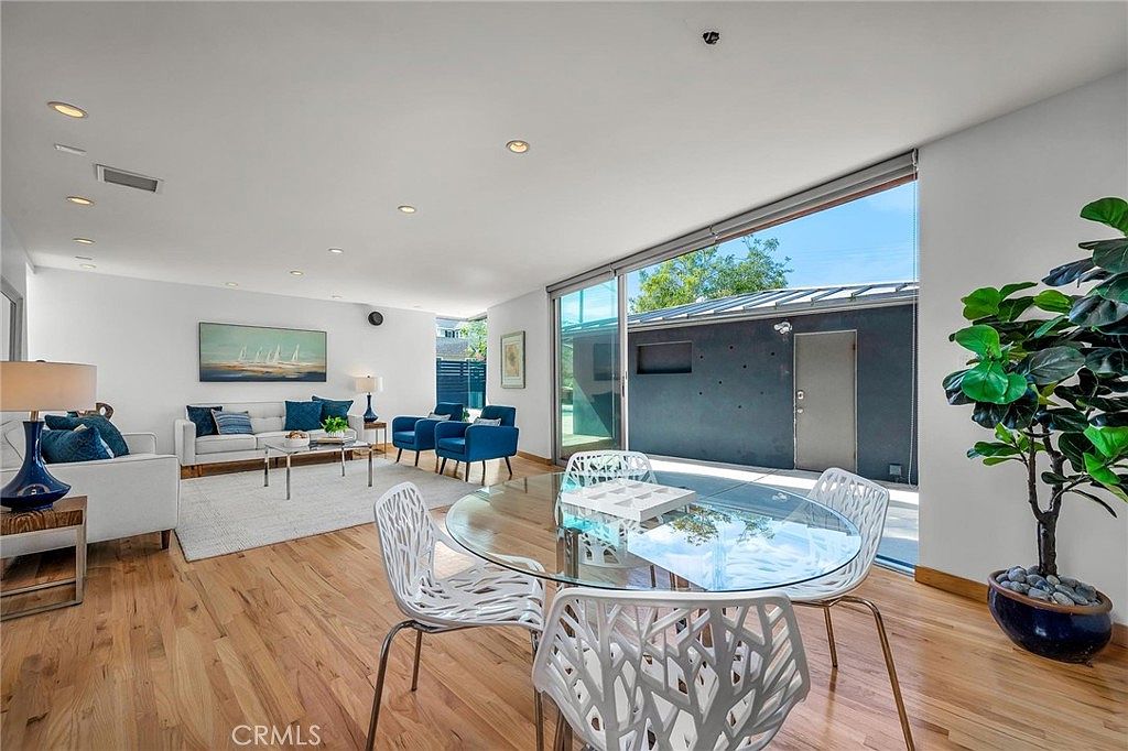Open living and dining with fiddle-leaf fig, white oak floors, and glass door to courtyard.